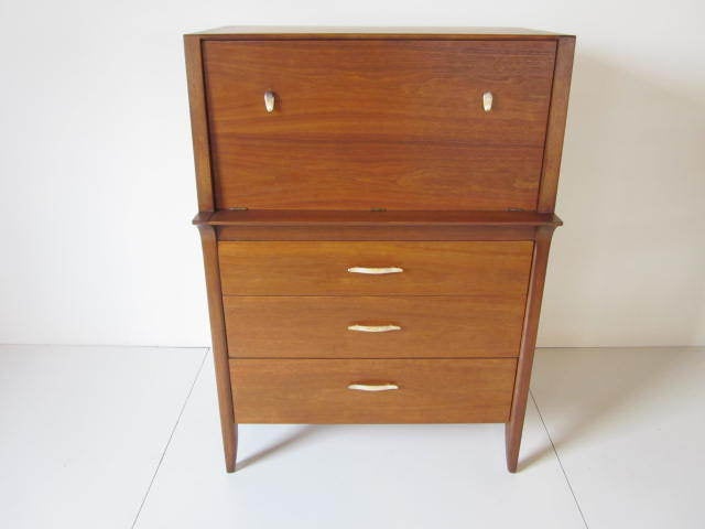 A three drawer chest with pull down desk top which reveals two middle drawers for storage and four white bent wood pull out files.Accented with bronze toned metal handles and refinished in a medium colored tobacco stain,retains branded mark