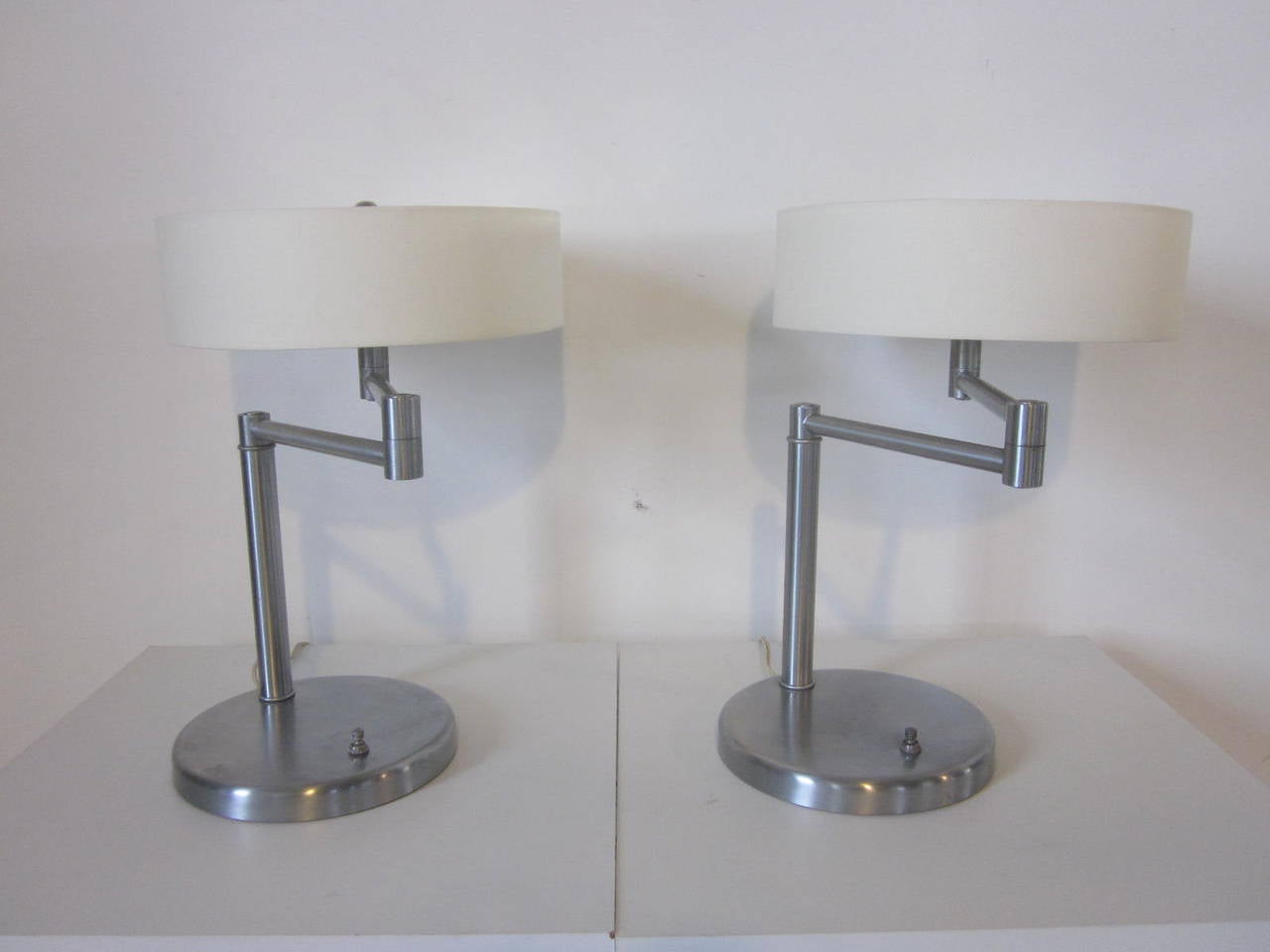 A pair of Nessen swing arm table lamps in brushed stainless steel with linen shades, opaque Lucite diffusers and stainless finials. Manufactured by the Nessen Lamp Company, NY.