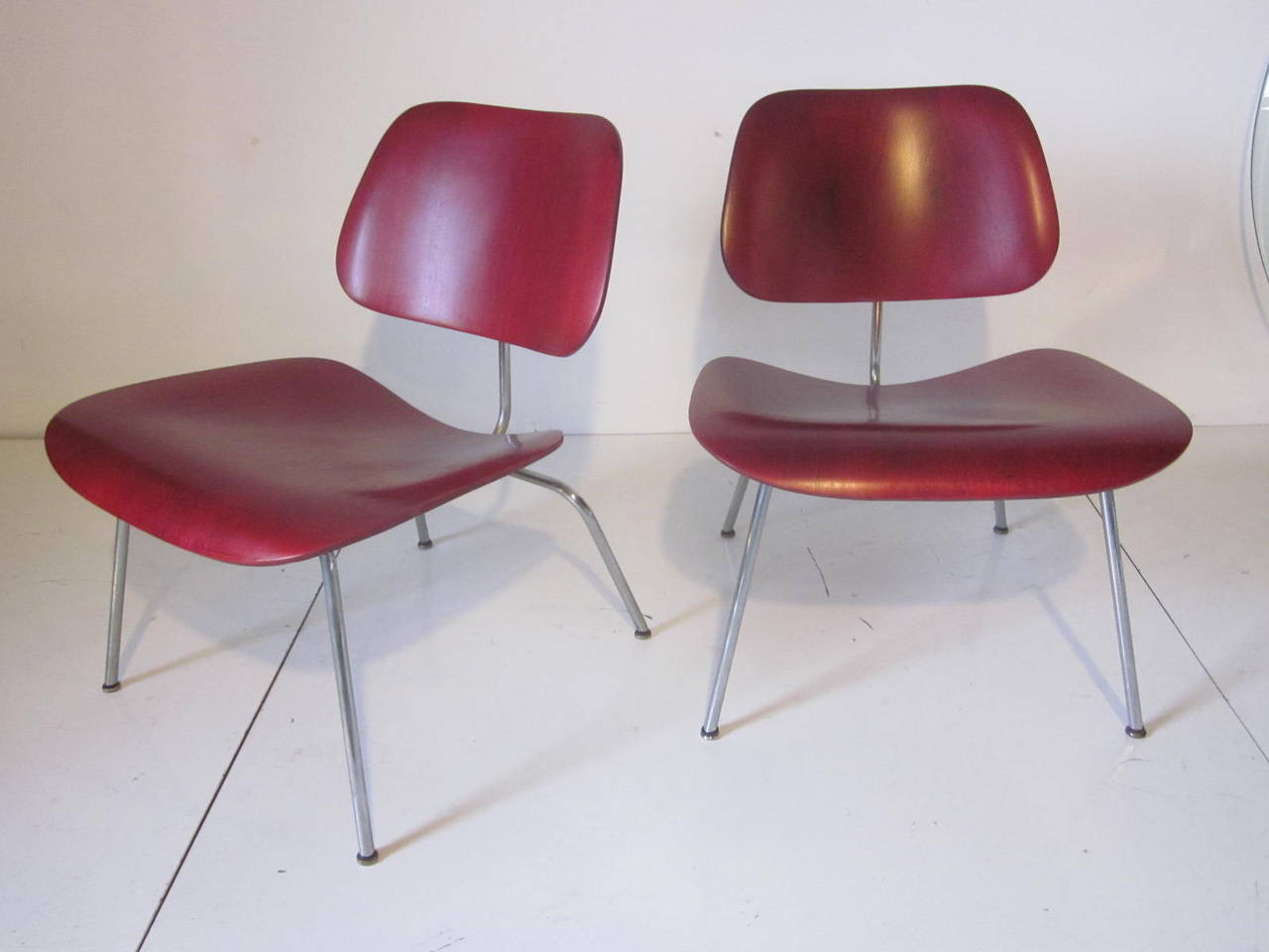 A pair of early original aniline dyed LCM (lounge chairs metal) bases with the early feet that screw into the legs, in a warm red on molded plywood. Manufactured by the Herman Miller Furniture Company.