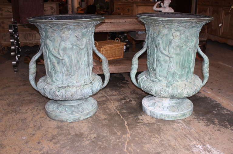 Pair of mid 20th-century urns in bronze. These substantial urns would be the perfect planter for a garden or patio. These elaborately detailed urns would make a welcoming statement framing a front entrance way. The urns are Grecian themed depicting