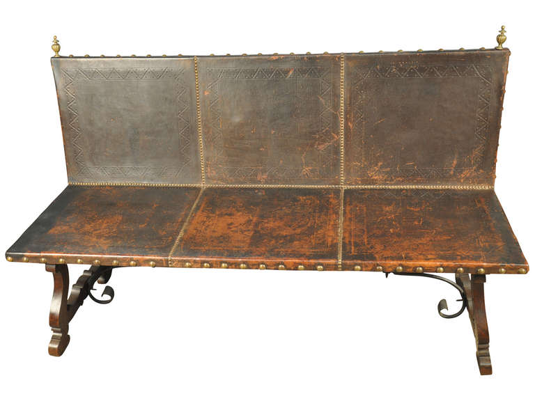 A very handsome Spanish Baroque style leather sofa - banquette - constructed from walnut with hand forges iron stretchers - and decorated with wonderful brass nail heads and finials.  This type of bench is rare and will lend elegance to almost any