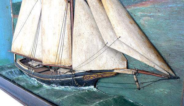 This is a wonderful example of a very rustic sailor made shadowbox or diorama of a two masted, gaff rigged, black hulled, schooner flying the American flag. Painted in the backboard, as if flying from the  foremast truck, is the owner's pennant, and