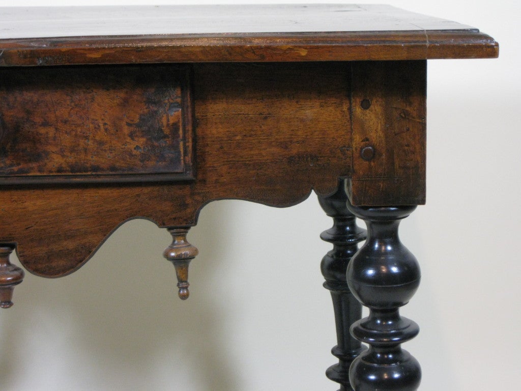 Flemish Baroque walnut side table with central drawer and ebonized base.