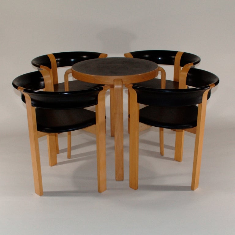 A set of 4 chairs and a small round table by Rud Thygesen and Johnny Sørensen for Magnus Olesen. The distinctive feature of these chairs is their unique design – half-circle back/arm rests made of thick laminated wood,; leather covered seats and 3