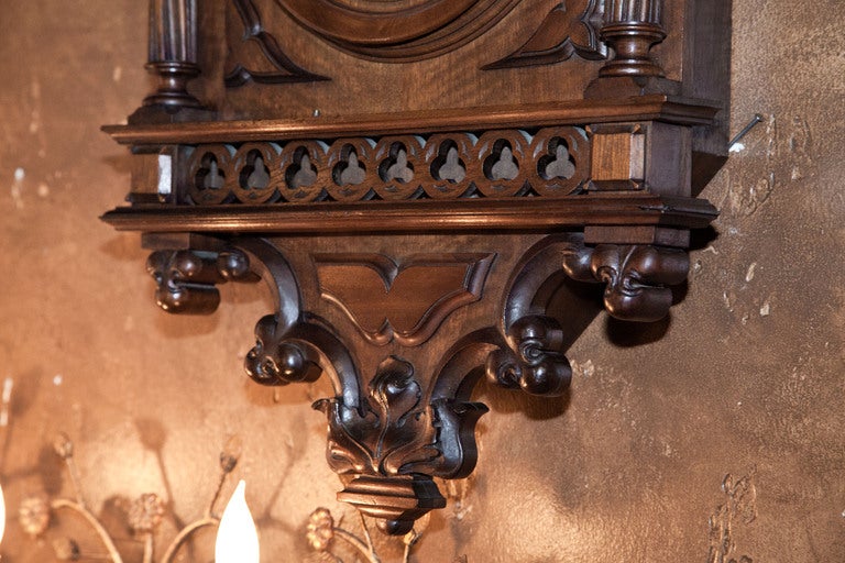 This stunning work was sculpted from select French walnut in the timeless Gothic style by obviously talented artisans! Stylized fleur de lys castellations and spires atop the boldly molded crown oversee thte clockface fitted with Roman numerals