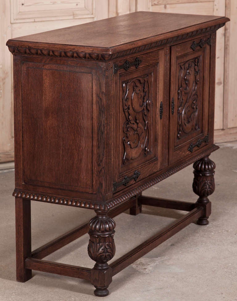 This Vintage Renaissance Raised Buffet was carved from solid oak to last for generations!  Raised upon carved urn pediments, it has been carved to perfection and accented with forged iron strap hinges and keyguards.  Being just under four feet in