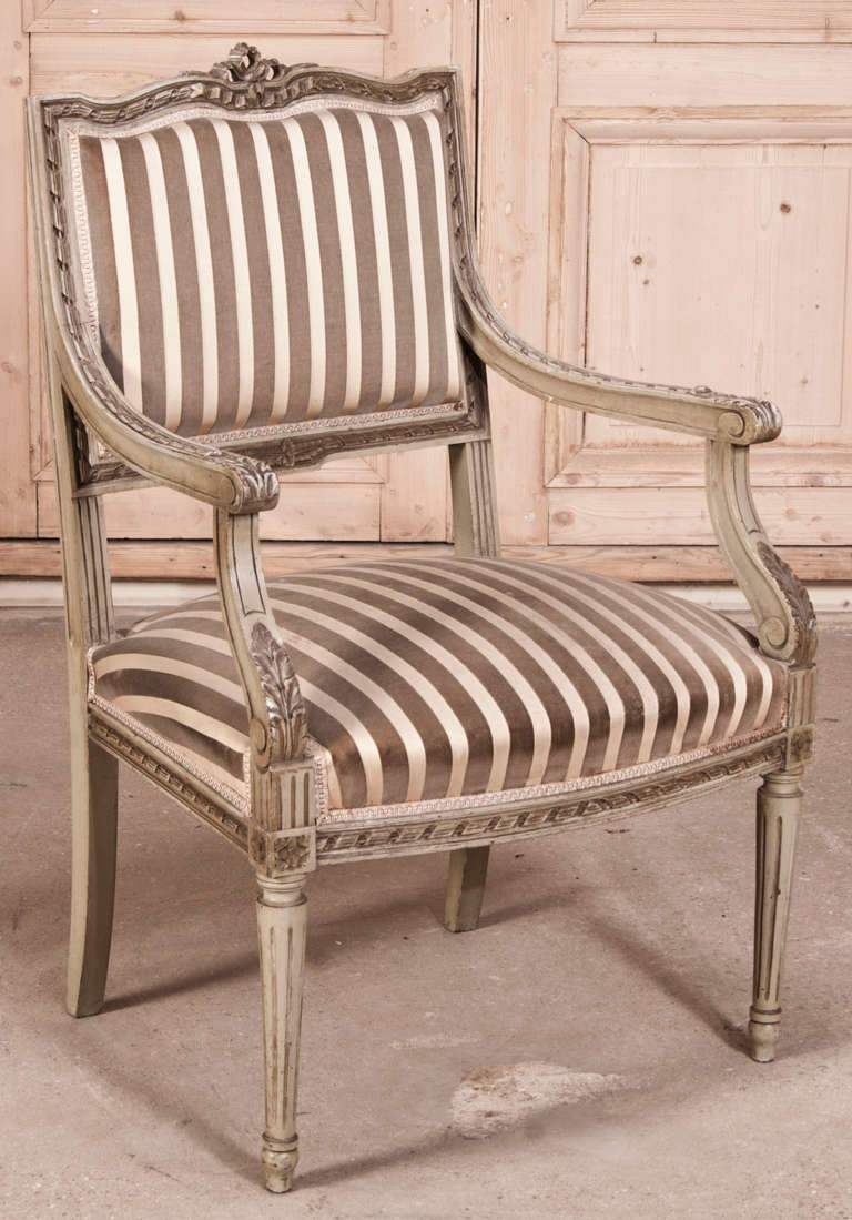 Pair Antique French Louis XVI Armchairs feature hand-carved artistry from the arched bow seatback crown with two types of ribbon motif, down the graceful armrests to the tapered & fluted column legs.  Acanthus leaf motifs provide additional accents,