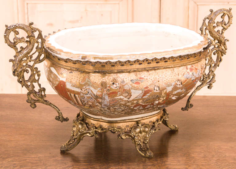 Crafted in the Orient for export to Europe, this Antique Oval Oriental Porcelain Jardiniere features a cast bronze rim, elaborate handles and an intricate base.  The colorful hand-painted designs were in great demand during the second half of the