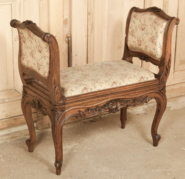 Hand-crafted from fine French walnut, this Antique Louis XV Armbench cleverly conceals a concealed bidet inside!  The perfect dual-purpose vanity bench when it was originally designed, it has been lavished with hand-carved detail on its undulating
