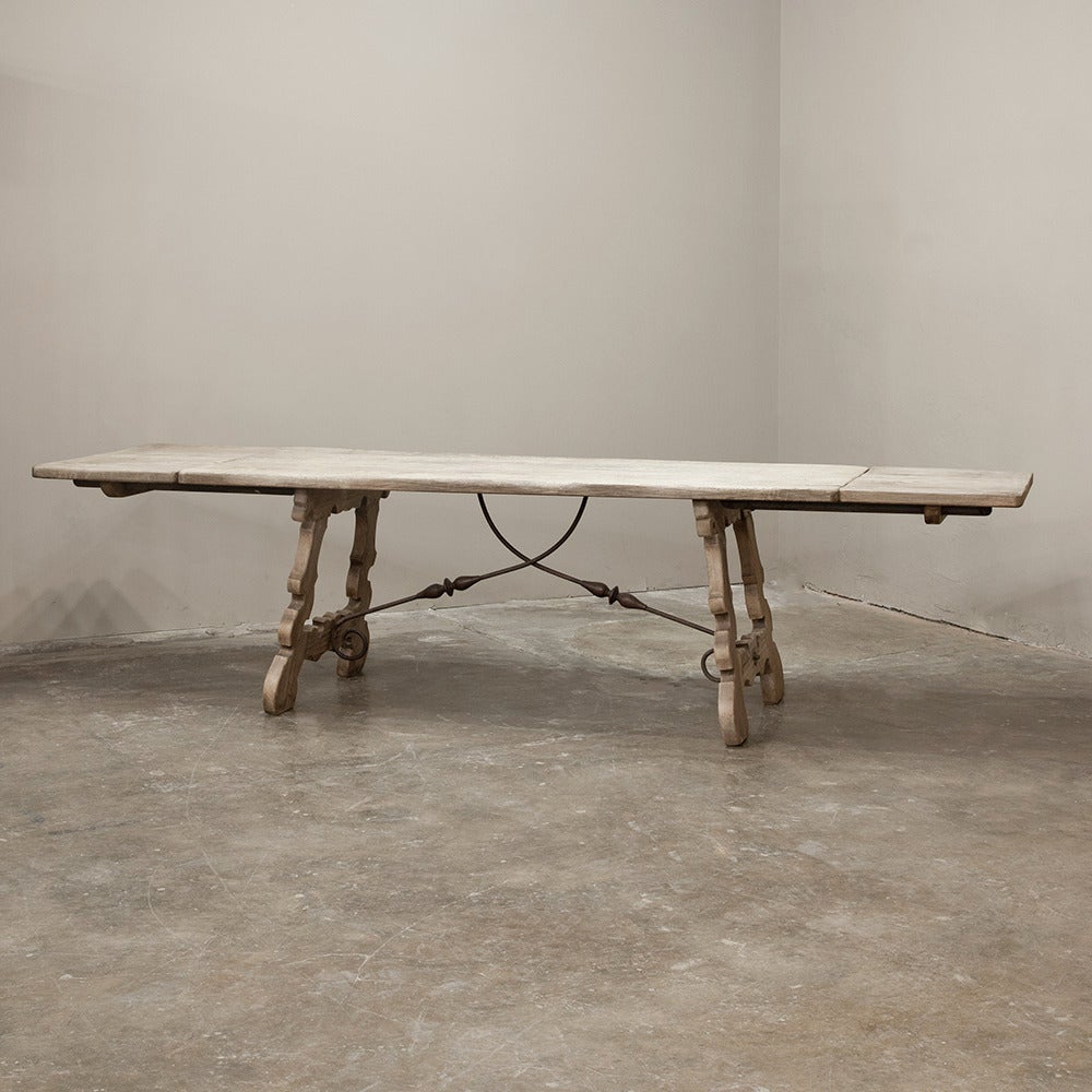 The lovely bandsawn legs and scrolled ironwork of this table are a result of a talented Spanish woodworker, indeed! This table exudes a rustic elegance owed to its intricately band-sawn supports, comfortably recessed and connected to the top via