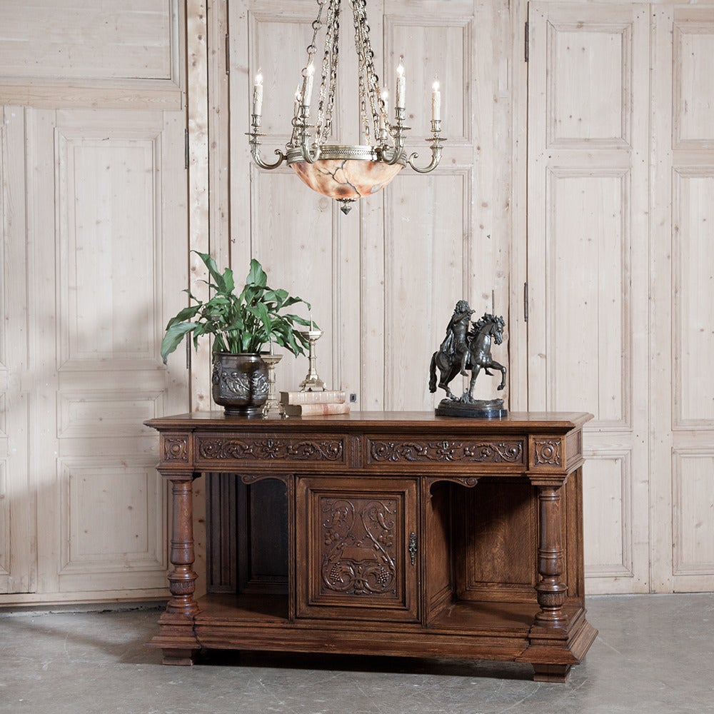 Sporting two display galleries on either side of the single cabinet, this interesting antique Renaissance buffet has also been carved with stylized foliate and olive motifs, complementing the carvings on the drawer fronts. Massive solid oak columns