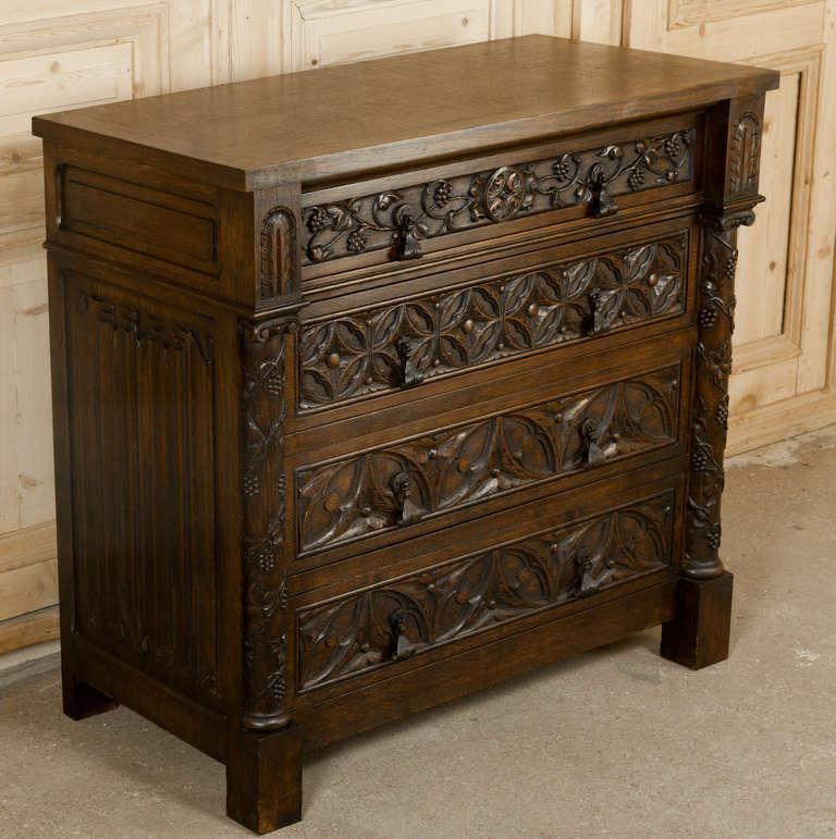 This Antique Gothic Commode features incredible carved detail from the richly crafted linenfold side panels to the geometric designs on the three lower drawers and finally to the fully laden grapevines depicted winding around the corner columns and