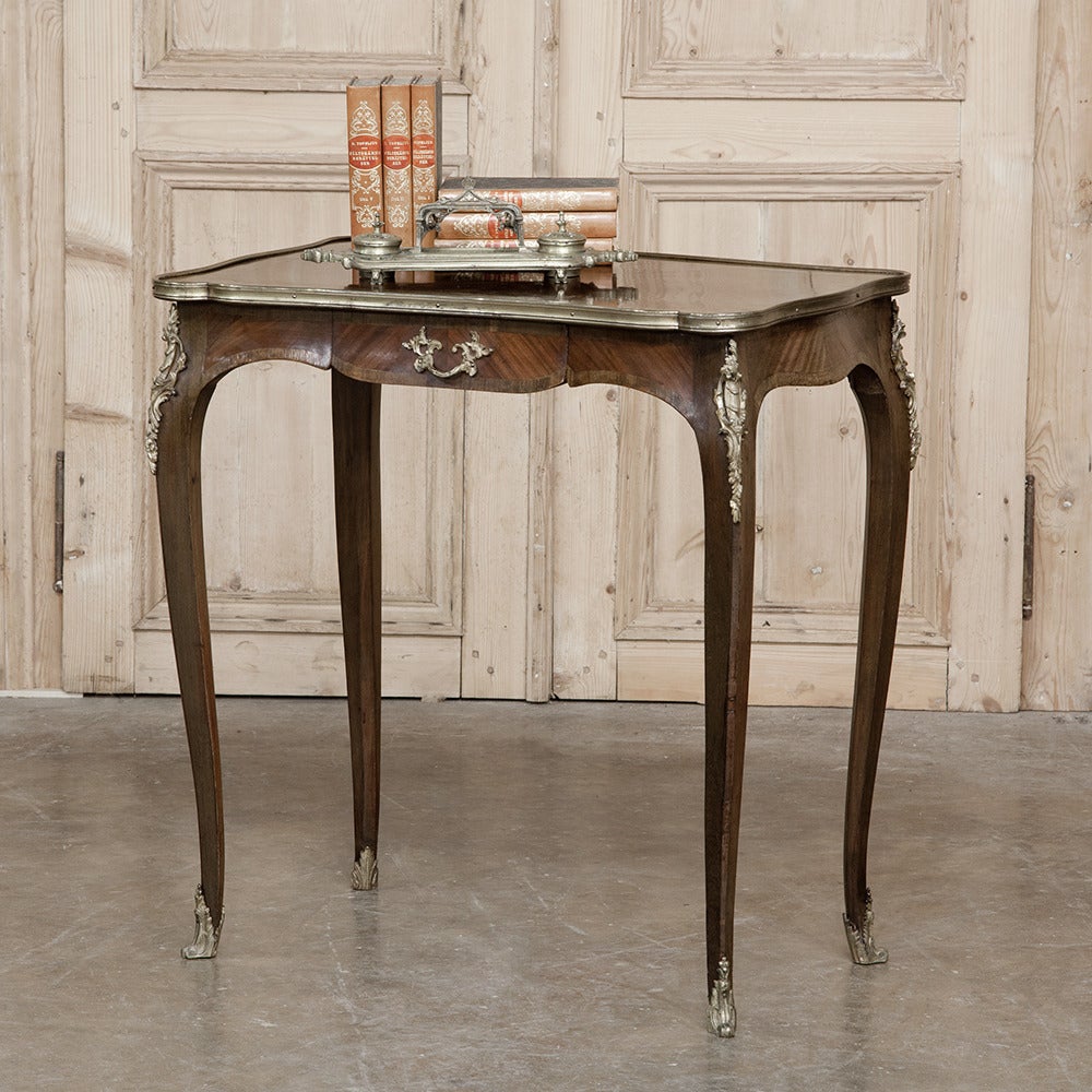 A lovely French Marquetry and Bronze Ormolu End Side Table in the Rococo style that so enamored Louis XV, was crafted during the late 19th century and features a rounded mahogany and rosewood top with a brass border. A rococo scroll-shaped apron
