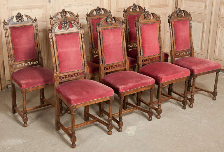 Set with heraldic crests carved into the arched seatback crowns, this set of eight chairs were crafted from fine French walnut with classical lines that never go out of style. Velvet upholstery is in serviceable condition. 
Circa 1870. 
Each