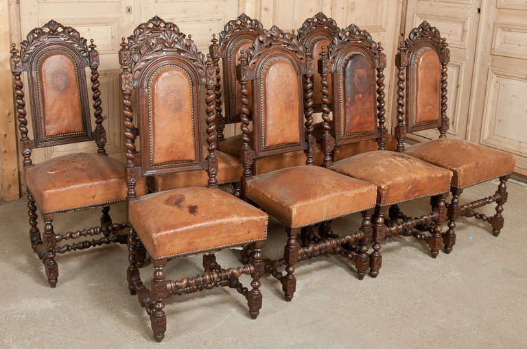 This set of chairs with barley twist frames from top to bottom, features bold foliate motifs creating a crown on the arched seatbacks, flanked by turned finials. The embossed leather backs are serviceable, but the seats will need reupholstering.
