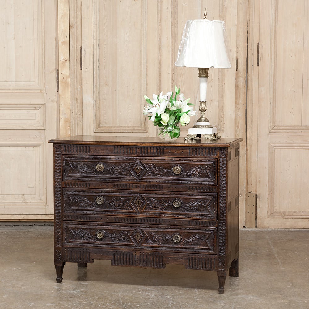 Handcrafted from solid old-growth French oak, this handsome 18th century country French commode features hand-carved adornment across the entire facade, punctuated by brass pulls. In particular, the three drawers have been carved in foliate bas