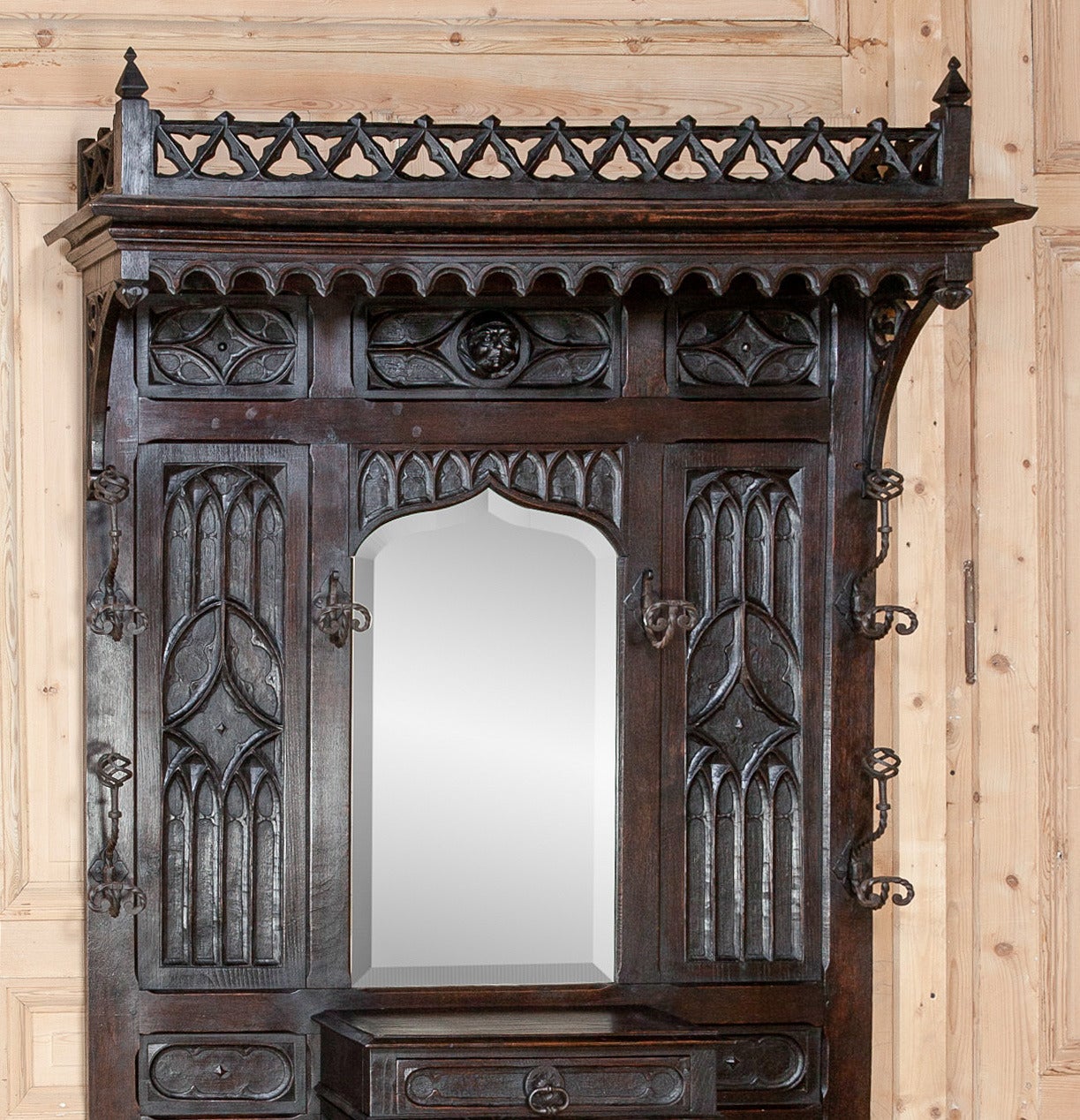 Handcrafted from dense, old-growth oak, this handsome, French Gothic hall tree features its original hand-beveled mirror and wrought iron hangers and umbrella rack! A simplistic interpretation of the style includes trefoils pierced into the crown's