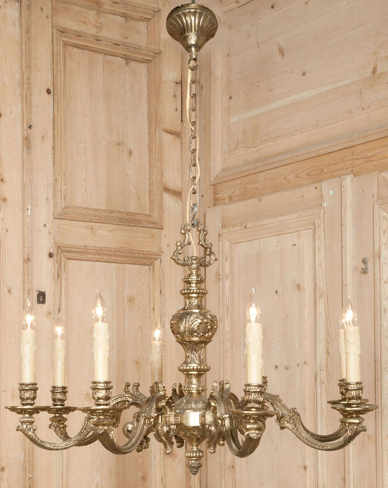Cast from solid brass in an intricate expression of the Regence style, this elegant chandelier boasts elaborate foliate motifs from the candle bases to the pendant finial, even up to the top of the chandelier where the primary chain attachment is