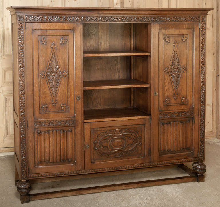 Fashioned from solid oak in the timeless Renaissance style, this impressive bookcase was produced during the revival that occurred in the early 1900s.  Linenfold panels below the elaborate rosettes on the  upper door panels also flank an intriguing
