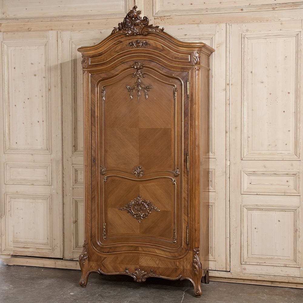 Resplendent with exceptional hand-carved detailing from the boldly arched crown to the intricately scrolled base, this stunning 19th Century French Walnut Armoire was styled in the manner of the Rococo, popular during the reign of Louis XV, and