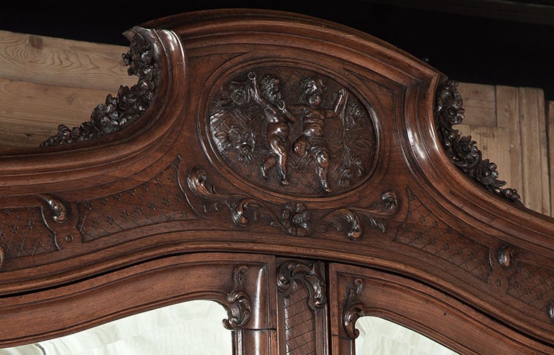Sculpted from select French walnut to last for generations, this stunning armoire soars to nine and a half feet high, and is topped with a sculpture of two companion cherubs, an indication that this could have been a wedding or anniversary gift. The