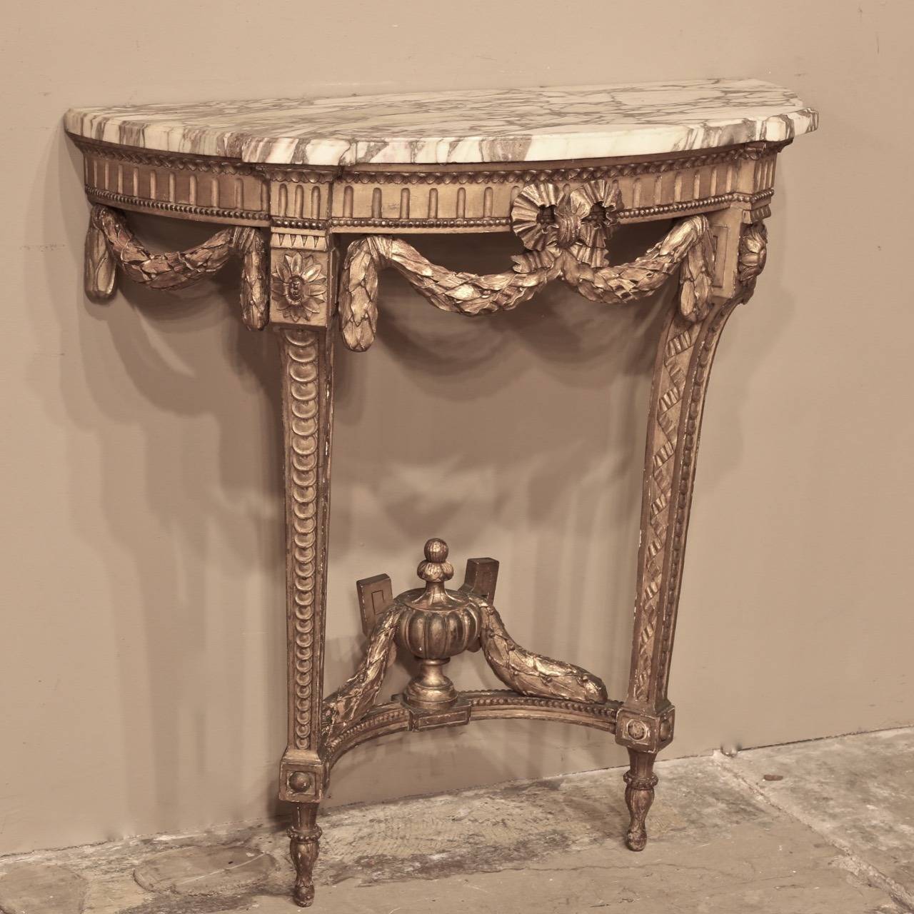 Resplendent with neoclassical style fervor, this magnificent Nineteenth Century French Louis XVI Giltwood Console has been carved with timeless laurel swags, urns and floral accents, and is topped with its original contoured and beveled marble. 