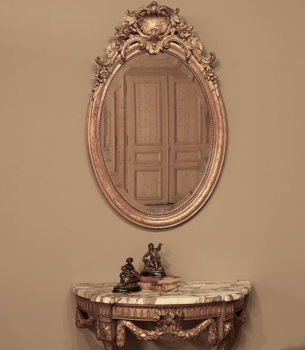 Elegant 19th Century French Neoclassical Gilded Oval Mirror adds beauty, form and function to any room! Featuring a shell cartouche on top lavished with floral and foliate motifs that cascade down the oval frame, which in turn features a subtle