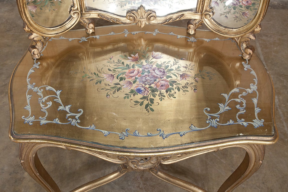 Boasting its original tri-panel mirror with the side mirrors on hinges to afford a reflection from three different angles, this exquisite 19th Century Italian Giltwood Vanity was hand-carved by master Italian craftsmen in the Rococo style, and