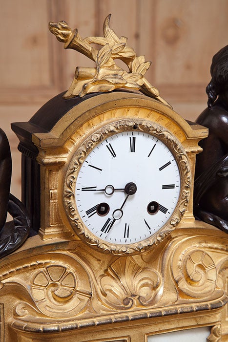 Cast from solid bronze and fitted with Cararra marble insets, this mantel clock features a hand-painted porcelain clockface dial and is in working order! Bell rings on the hour with a delightful peal. Blackened bronze casework is designed to mimic