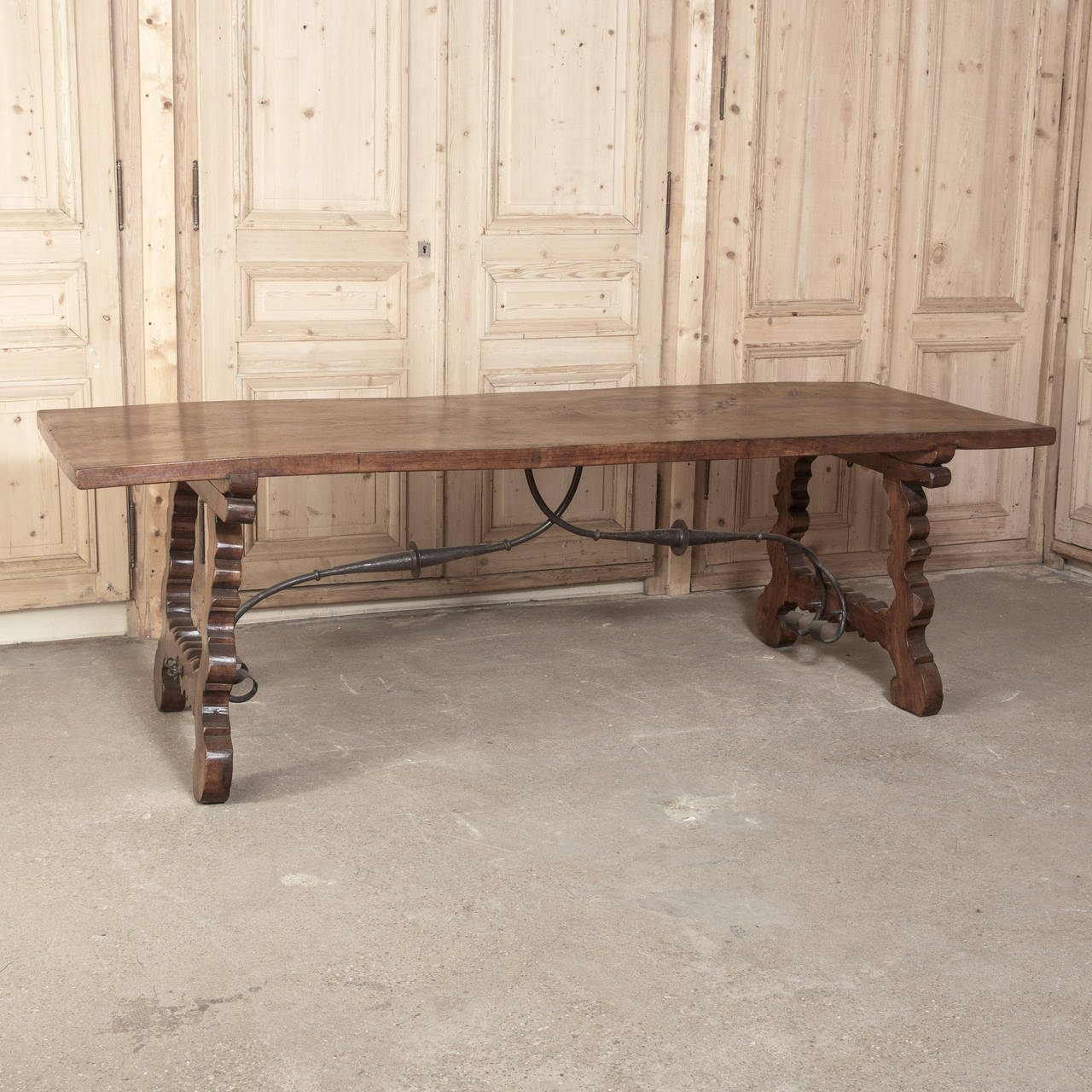 Hand-crafted by master Spanish artisans from Walnut harvested from the Pyrenees, this Antique Dining Table features the classic bandsawn side supports that are dovetailed into the solid plank top.  The wrought iron stretchers below add graceful