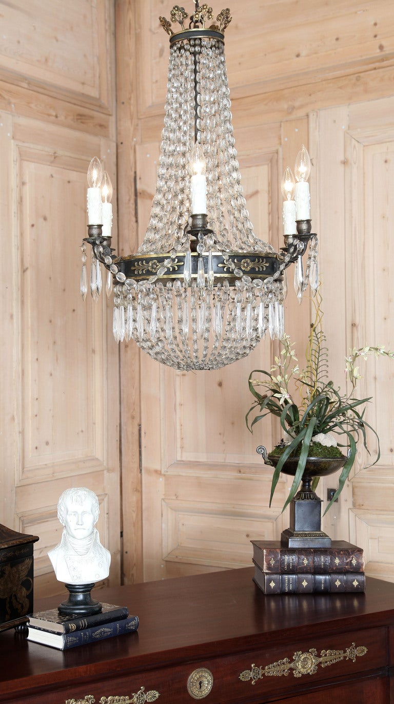 Featuring a bronze carriage with its original black enamel paint punctuated by French Empire period castings, this chandelier offers grandiose flair in a more manageable size. The magnitude of multi-faceted crystals forming the timeless 