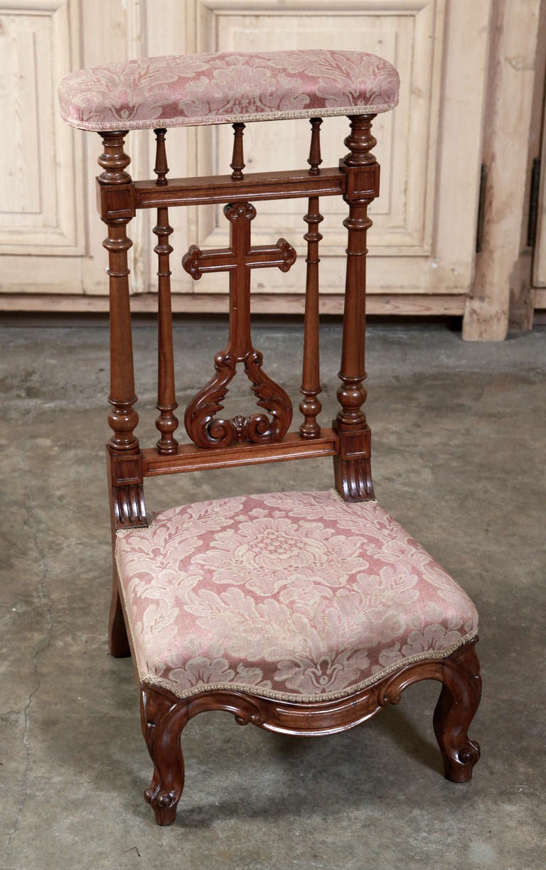 Sculpted from select French walnut, this prie dieu features a depiction of the cross surrounded by columnar architecture, with its silk brocade upholstery apparently in very serviceable condition. Perfect for a cozy niche devoted to prayer. 
Circa