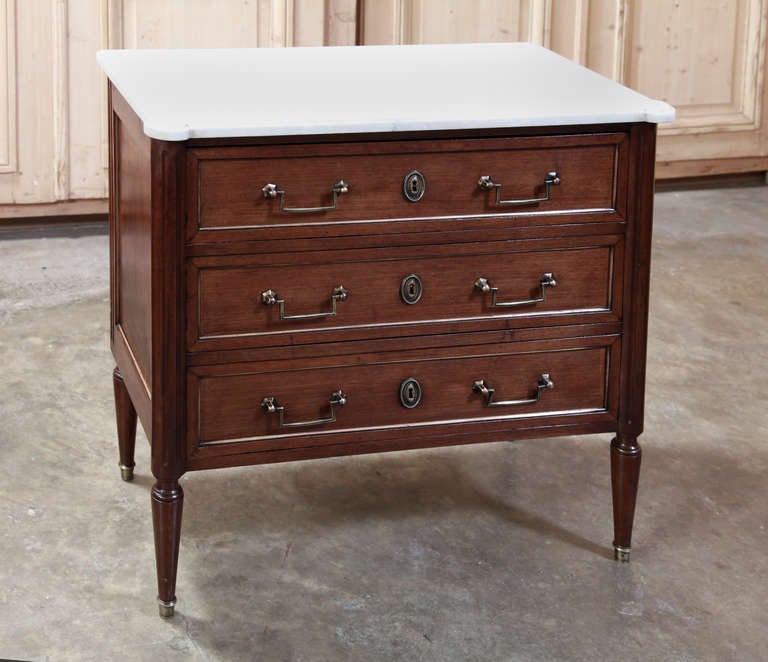 Crafted from exotic imported mahogany then trimmed with brass molding and fitted with brass pulls and keyguards, this tailored commode has been topped with beveled Cararra marble. 
Circa 1900-1910. 
Measures 31 x 32.5 x 16.5.