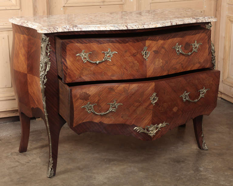 Antique French commode was crafted in the Louis XV bombe style and is lavished with marquetry, cast bronze ormolu and pulls, and a contoured & beveled marble top.  The result of four master artisans, such commodes are truly a marvel.  First the