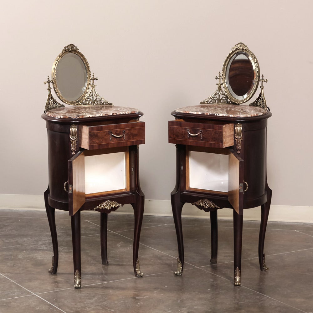 Combining burl walnut panels with exotic rosewood inlay to create artistic expressions, known as marquetry, this pair of antique French Louis XVI nightstands features finely cast bronze neoclassical supports for oval vanity mirrors overlooking the