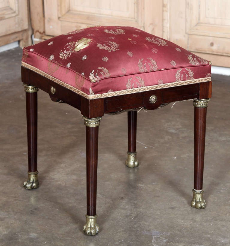 Rendered from exotic imported mahogany by master French artisans, this footstool has been mounted with bronze ormolu in the manner of the First Empire, but during the reign of Bonaparte's successor Napoleon III. Original silk upholstery has not