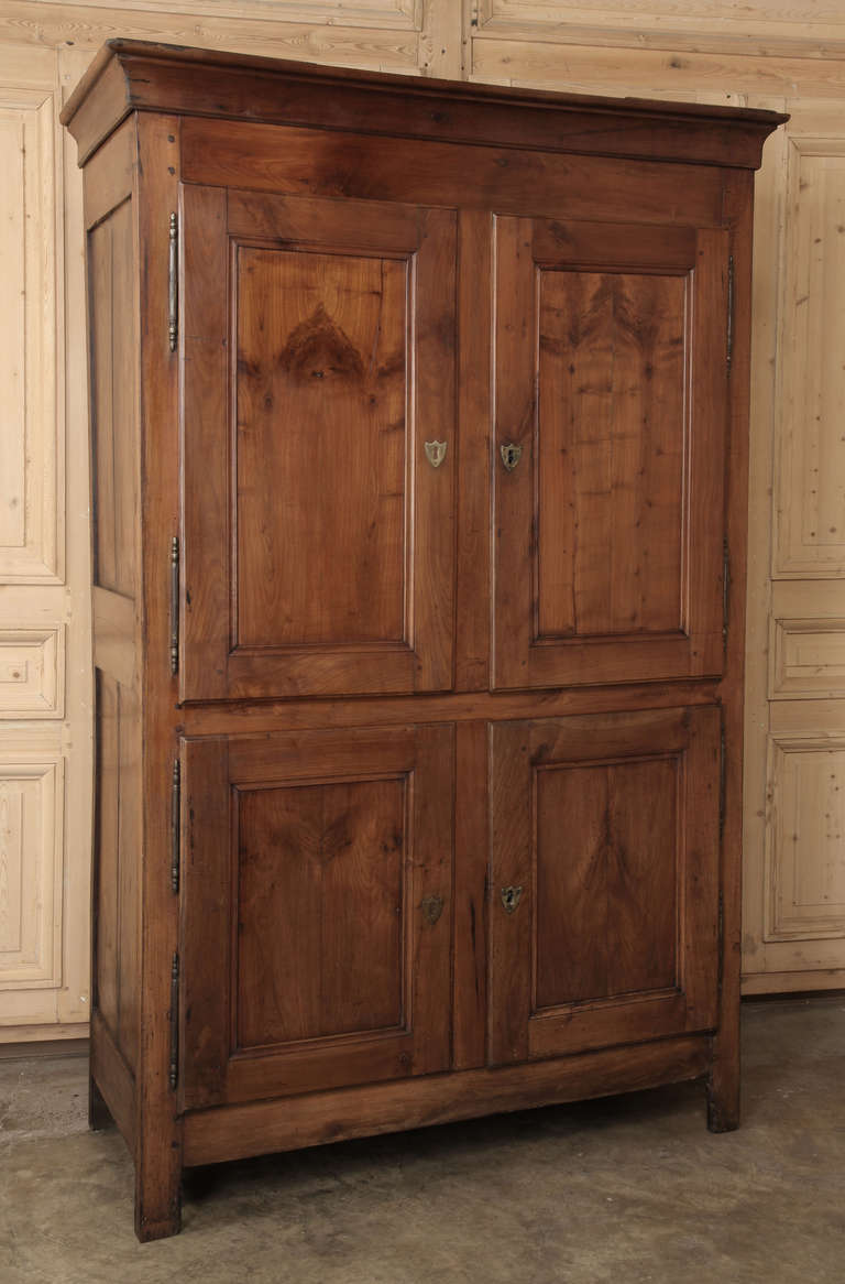 Featuring an austerity of line and form executed in solid cherry wood that has achieved a lovely patina in the last century and a half, this Antique French Louis Philippe 4-Door Armoire has four doors to add convenience. Original brass hinges and
