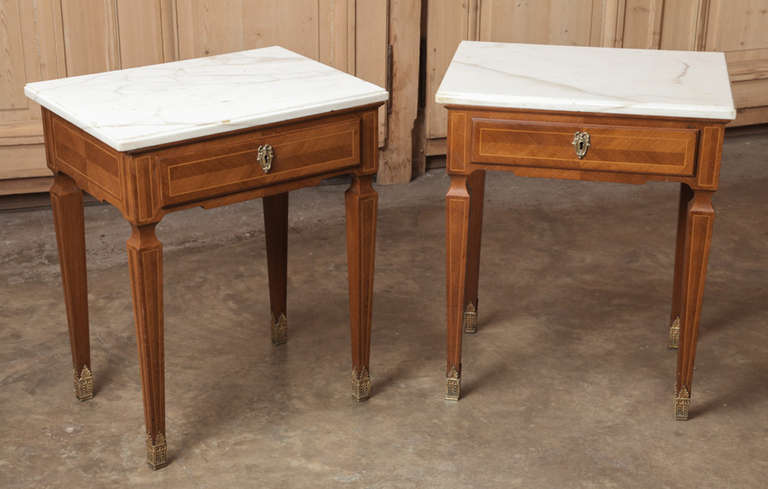 Featuring simplistic architecture rendered with restrained elegance, this Pair of Antique French Marquetry Marble Top Nightstands are perfect for seating groups or as bedside companions, with Cararra marble tops for carefree opulence.  Inlay and