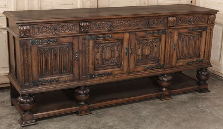 Fashioned from solid oak, this Vintage Raised Gothic Buffet is supported on massive carved urns which also define a lower exposed shelf.  The forged strap hinges complement the carved facade very nicely, and the surface is broad enough to serve a