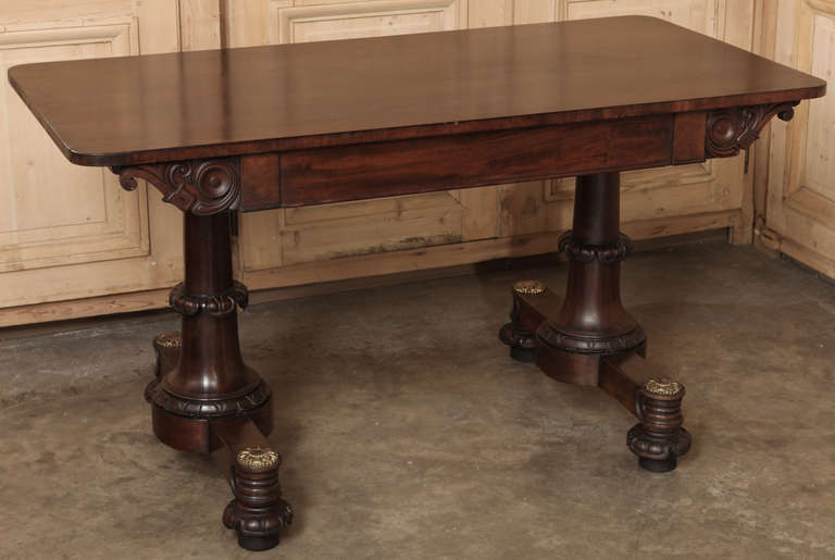 An ideal choice for the 21st century office or your home office or library, this Antique English Writing Table was styled in the Georgian manner from fine imported mahogany, and boasts cast bronze rosettes atop a tastefully carved column and foot