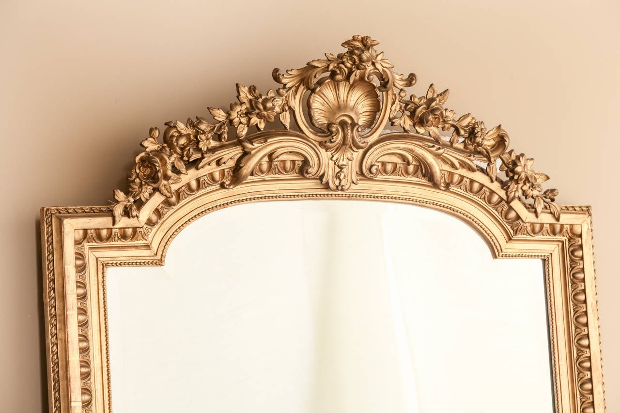 Featuring Classic and Baroque motifs that are symmetrically applied across the entire arched crown, this exquisite antique Regence French gilded mirror will add opulence to any room! Shell, floral and foliate motifs abound on the crown, while the