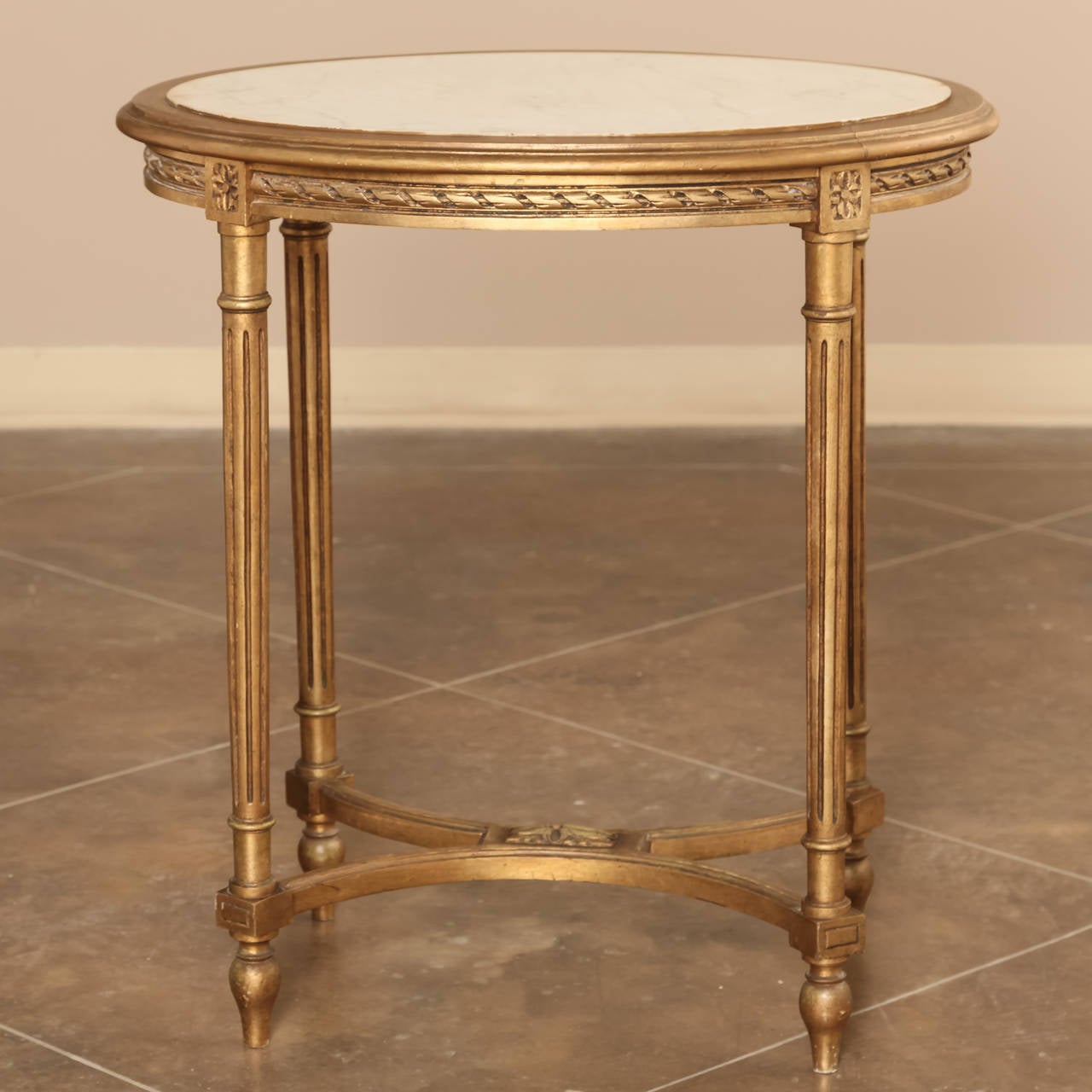 Add elegance to any room with this Classic oval occasional table, handcrafted in the Louis XVI style then given a gold finish and Carrara marble top for the ultimate in carefree opulence. Tapered and fluted legs connected with bowed stretchers