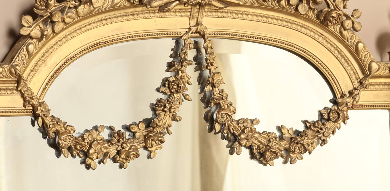Resplendent with exquisite renderings that define the classical style, this impressive Louis XVI gilded mirror features its original beveled glazing. A floral wreath with sprays adorns the arched crown, set with the torchere and carquois de fleche