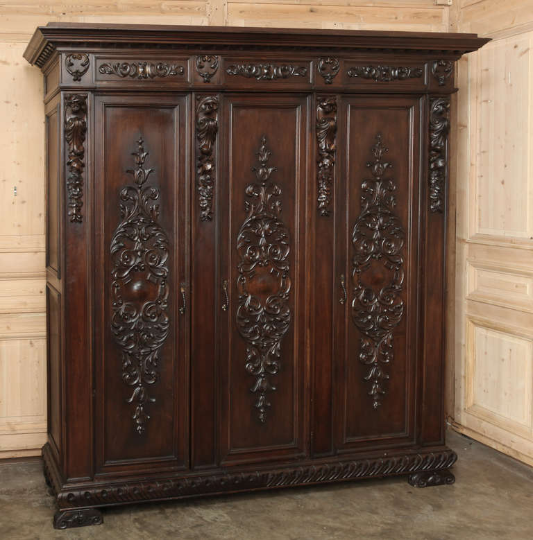 Benchmade from fine Italian walnut and hand-carved with a glorious expression of Renaissance-inspired embellishment in full relief, this triple armoire will provide copious amounts of stylish storage. Heraldic crests centered on the door panels are