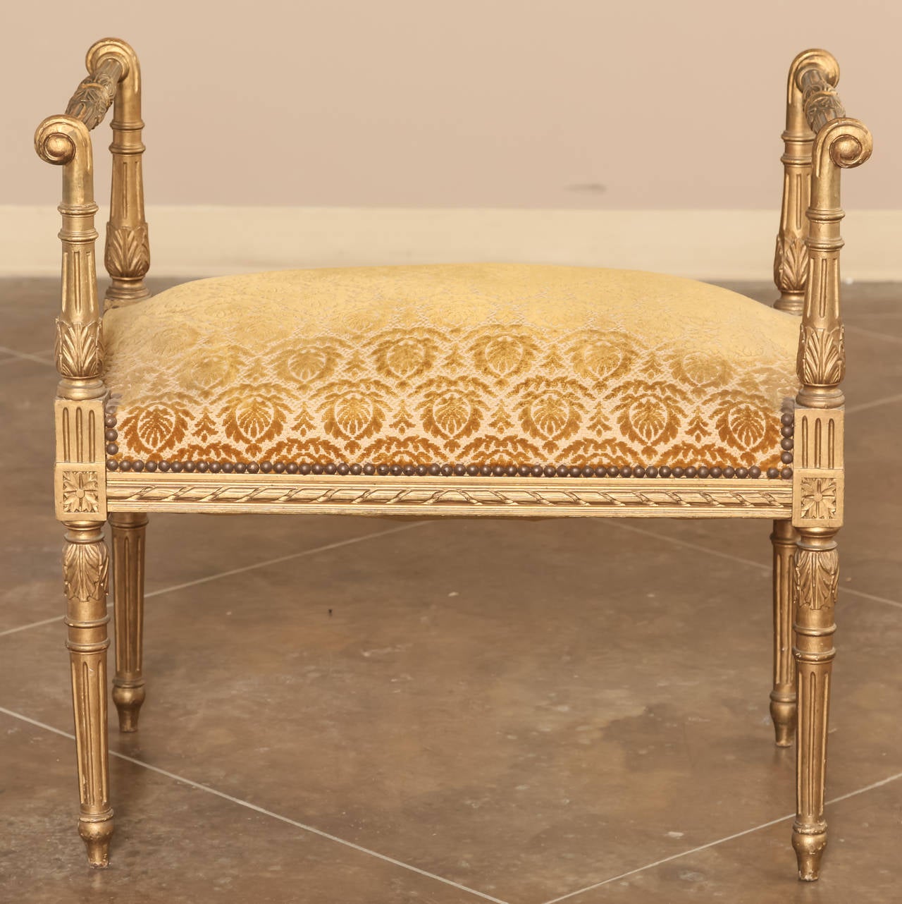 Louis XVI gilded vanity bench is a great choice for the bathroom, bedroom, or anywhere an elegant bench is needed. Classical styling with tapered and fluted columns catches the eye, while the gold finish adds opulence. Upholstery is in serviceable