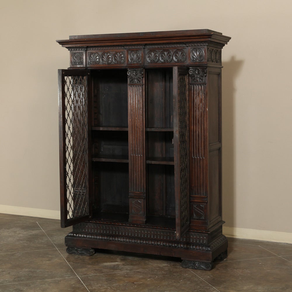 Handcrafted from fine Italian walnut by master artisans, this antique Italian neoclassical bookcase features elaborate shell carvings across the crown, accentuated by detailed molding, and presiding over the lower display portion. The display