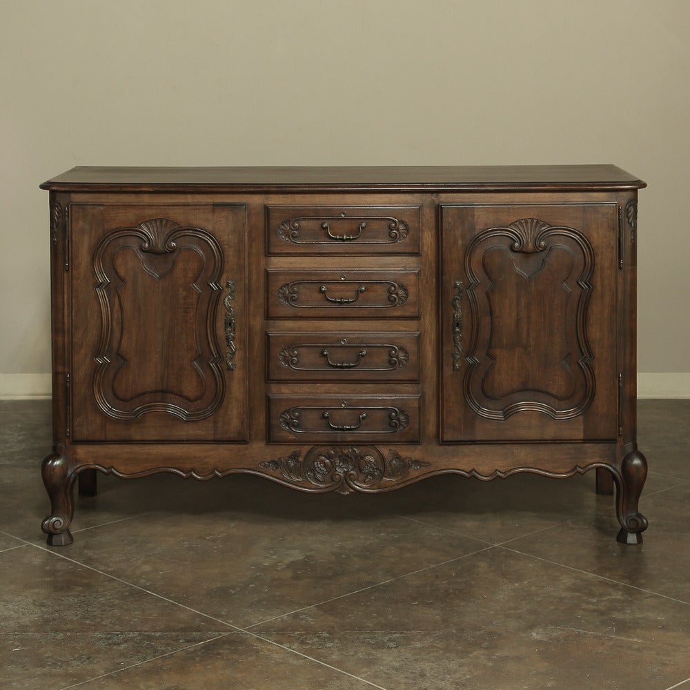 Rendered from solid French walnut-this charming Country French buffet features two spacious cabinets flanking a center tier of four drawers, all carved with scrolled frameworks and fitted with forged steel hardware. Scrolled apron and legs provide