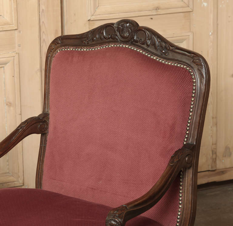 This Pair of Antique French Louis XV Walnut Armchairs exude comfort thanks to the upholstered, padded enclosed sides and plush cushioning.  Called bergeres by the French, each was sculpted from fine French walnut and hand-carved with embellishments