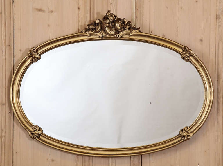 A superb choice for bath or powder room, or in the salon to reflect the remainder of your lovely room, this oval beveled mirror is surrounded by a giltwood frame carved with stylized shell and foliate motifs in the classic rococo manner.