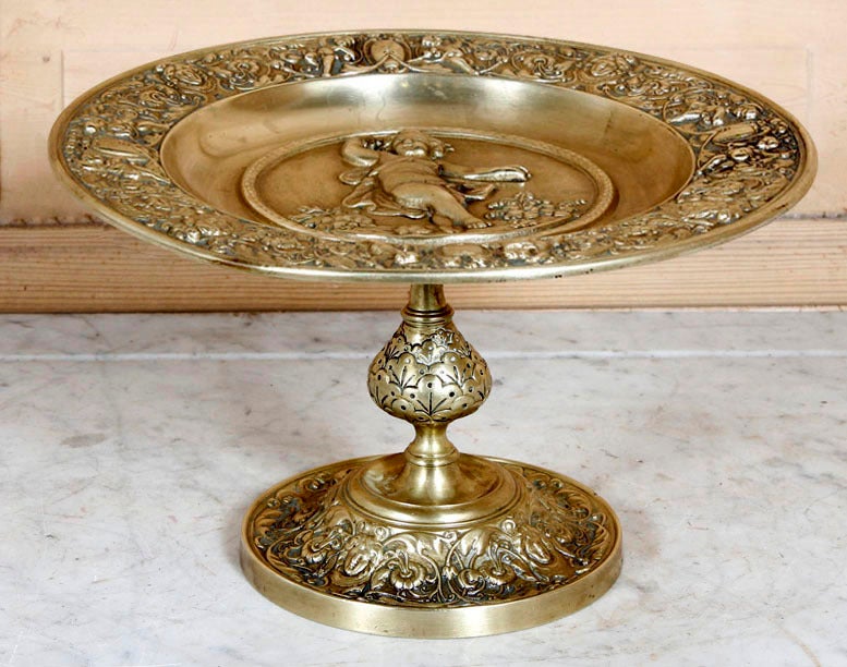 Serve your finest in style on this elegant bronze compote, rendered in magnificent relief with intricate designs inspired by the Renaissance, and centered with a dancing cherub. Such keepsakes were designed to be decorative when not in use, hence